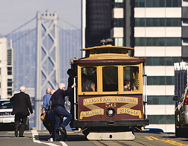 Cable car and passengers on Nob Hill along California Street, with west span of the Bay Bridge in background, San Francisco, California, United States of America, North America