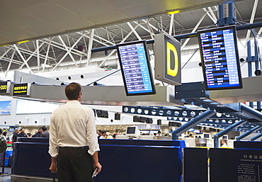 A airline traveler in an airport reading the plane departure signage, Beijing, China, Asia