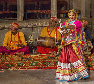 An Indian woman wearing a multi-coloured costume performs a Rajasthani folk dance, with musicians playing acoustic instruments, Udaipur, Rajasthan, India, Asia