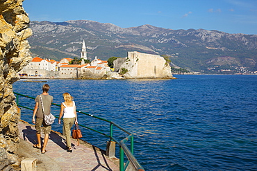 Couple walking along coast towards Old Town, Budva, Montenegro, Europe