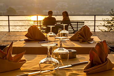 Restaurant tables set for dinner and couple overlooking lake at sunset, Como, Province of Como, Lake Como, Lombardy, Italian Lakes, Italy, Europe