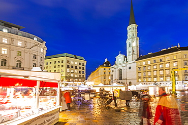 View of Christmas Markets stalls and St. Michael Catholic Church in Michaelerplatz at dusk, Vienna, Austria, Europe