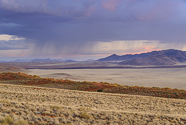 Some much needed rain falls in the distance at dusk in NamibRand Nature Reserve, Namib Desert, Namibia, Africa