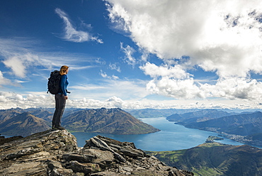 Woman on top of a mountain, view on Lake Wakatipu with city of Queenstown, Remarkables mountain range, South Island, New Zealand