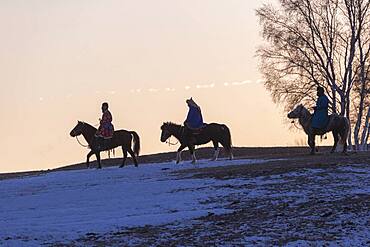 three Mongolian horsemen on a horse running in a meadow covered by snow, Bashang Grassland, Zhangjiakou, Hebei Province, Inner Mongolia, China