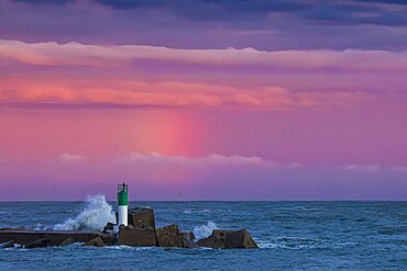 Waves breaking on the port light of the south entrance of the port of Sete at sunset, Herault, Languedoc-Roussillon, France