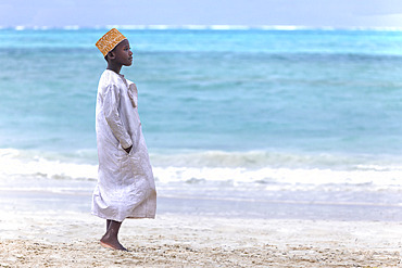 Little boy wearing abaya, white jdellaba and orange and gold kofia. In the late afternoon, children from a small village come to play on the white sand beach and turquoise sea on the east coast of Zanzibar, Tanzania.