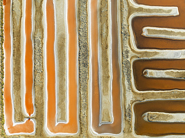 Saline ponds at the salt works near Chiclana de la Frontera. The orange-red colour depends on the level of salinity and is directly caused by the algae Dunaliella salina and brine shrimp. Aerial view. Drone shot. Cádiz province, Andalusia, Spain.