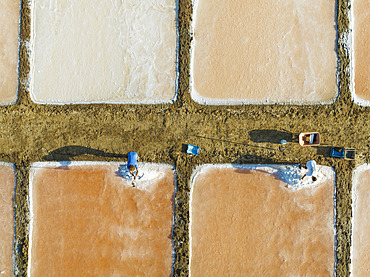 Harvesting salt at the saline ponds near Chiclana de la Frontera. The orange-red colour depends on the level of salinity and is directly caused by the algae Dunaliella salina and brine shrimp. Aerial view. Drone shot. Cádiz province, Andalusia, Spain.