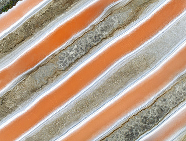 Saline ponds at the salt works near Chiclana de la Frontera. The orange-red colour depends on the level of salinity and is directly caused by the algae Dunaliella salina and brine shrimp. Aerial view. Drone shot. Cádiz province, Andalusia, Spain.