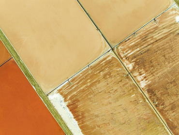 Saline ponds at the salt works next to Almadraba de Monteleva. The reddish colour depends on the level of salinity and is directly caused by the algae Dunaliella salina and brine shrimp. Aerial view. Drone shot. Nature Reserve Cabo de Gata-Nijar, Almería province, Andalusia, Spain.