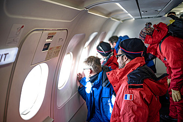 Team of Antarctic expeditionaries watching the landscape through the windows of the Airbus A320 carrying them from Hobart;Tasmania) to Mario Zucchelli;Italian coastal Antarctic base), as they approach the latter. These are the first summer campers. In red are those who will then take a Basler to the French coastal summer station of Cap Prud'Homme or Robert Guillard. They'll spend a few days opening it up and warming it up, before moving on to the Dumont d'Urville base;6km from Cap Prud'Homme), marking the end of wintering there. In blue: the expeditionaries bound for Concordia.