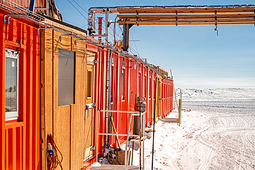 Building made of containers lined up in a row, powered by pipes and electric cables. The summer camp is made up of containers assembled together. It was built in the early 1990s. Since then, irregular ground settlement has caused the building to deform. It is now used as a summer dormitory. Concordia Antarctic Research Station, Dome C plateau, East Antarctica.