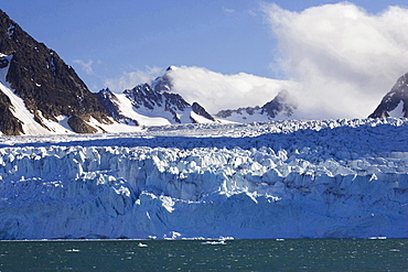 Monaco glacier front cliff on water fjord mountains in environment partially snow overcast