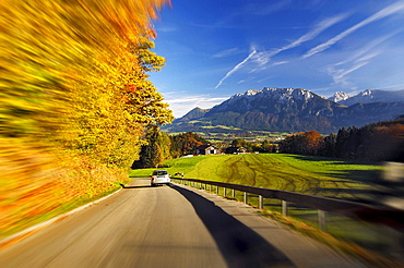 car driving on German alpine road at Bayrischzell colored trees on roadside landscape with mountains autumn mood