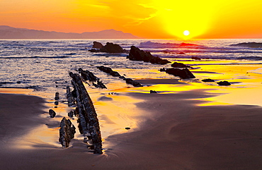 parallel rock formations on sea shore in tidal zone of sea with sun at sunset sunrise in background contre-jour shot backlit outdoors La Rasa Mareal flysch cliffs Basque Country Spain Europe