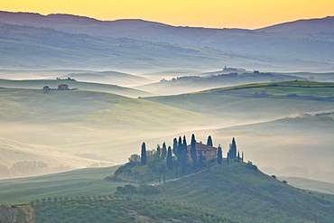 hilly landscape with wheat fields and cypresses surrounding traditional Tuscan stone house farmhouse nature morning mood