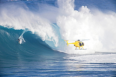 A helicopter filming a tow, in surfer at Peahi Jaws off Maui Hawaii