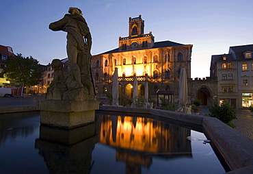 old historical neo-gothic illuminated city hall reflexion in fountain water of Neptune fountain on market place twilight mood