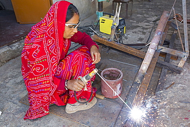 Women welding joints during the construction of solar cookers at the Barefoot College in Tilonia, Rajasthan, India. The Barefoot College is a worldwide charity, founded by Bunker Roy, its aims are, education, drinking water, electrification through solar power, skill development, health, women empowerment and the upliftment of rural people. Solar cookers save women having to walk to the froest to cut down wood for cooking, thus saving the forests, and a daily chore for woman.