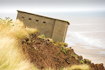 A Second world War lookout post leaning alarmingly and about to tumble over the edge of the cliff near Aldbrough on Yorkshires East Coast, UK. The coast is composed of soft boulder clays, very vulnerable to coastal erosion. This section of coast has been eroding since Roman times, with many villages having disappeared into the sea, and is the fastest eroding coast in Europe. Climate change is speeding up the erosion, with sea level rise, increased stormy weather and increased heavy rainfall events, all playing their part.