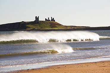 Spray in windy conditions from breaking waves, looking towards Dunstanburgh Castle, Northumberland, UK.