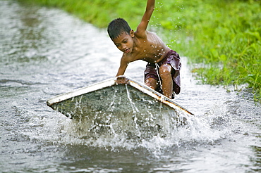 Boy playing in the floodwater caused by sea water incursion due to global warming induced sea level rise that threatens the future of these low lying islands, Funafuti Atoll, Tuvalu, Pacific