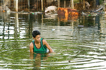 Boy wading in the floodwater caused by sea water incursion due to global warming induced sea level rise that threatens the future of these low lying islands, Funafuti Atoll, Tuvalu, Pacific