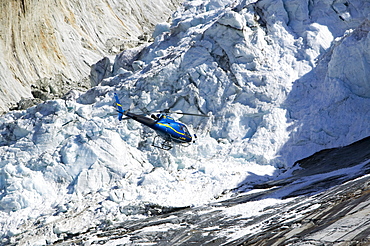 A tourist hericopter traverses melting seracs on the snout of the Argentiere Glacier, like most Alpine glaciers it is retreating rapidly due to global warming, Chamonix, Haute Savoie, France, Europe