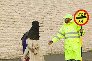 Pakistani women wearing the traditional burkha crossing the road in Burnley with the help of a lollipop man, Lancashire, England, United Kingdom, Europe