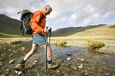 A walker uses trekking poles to help him cross the upper Esk in the Lake District, Cumbria, England, United Kingdom, Europe