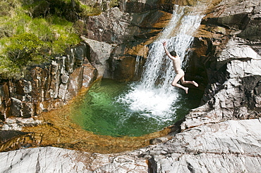 A man leaps into a plunge pool below a waterfall on the side of Ben Starav, a Munro in the Highlands, Scotland, United Kingdom, Europe