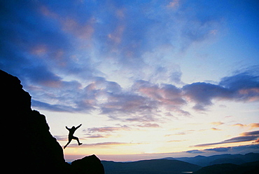 A climber jumping down a crag on Harter Fell at sunset, Lake District, Cumbria, England, United Kingdom, Europe