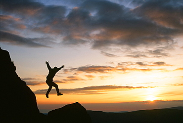 A climber jumping down a crag on Harter Fell at sunset, Lake District, Cumbria, England, United Kingdom, Europe