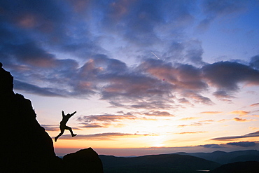 A climber leaping down a crag on Harter Fell at sunset, Lake District, Cumbria, England, United Kingdom, Europe