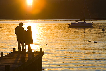 A couple on a jetty at sunset at Waterhead, Ambleside, Lake District, Cumbria, England, United Kingdom, Europe