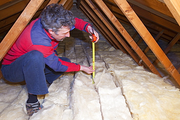 A man measuring the depth of insulation in a house loft or roof space