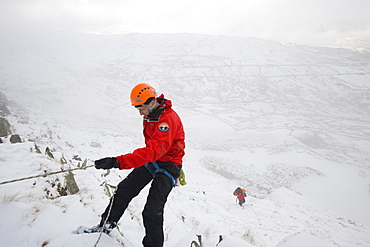 A mountain rescue team member abseiling in the snow above Kirkstone near Ambleside in the Lake District, Cumbria, England, United Kingdom, Europe