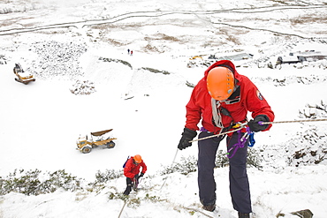 A mountain rescue team member abseiling in the snow above Kirkstone near Ambleside in the Lake District, Cumbria, England, United Kingdom, Europe