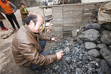 A man breaks up coal for domestic use, China, Asia