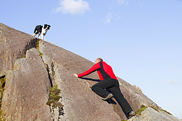 A climber and border collie dog on a boulder above Chapel Stile in the Langdale Valley in the Lake District, Cumbria, England, United Kingdom, Europe