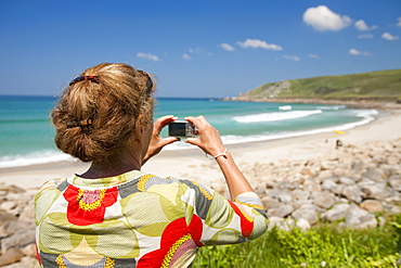 A woman takes a photograph of Nanven cove beach in Cornwall, England, United Kingdom, Europe