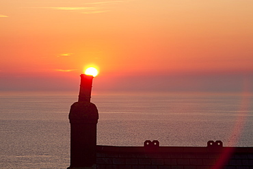 The sun setting over a house chimney at Cape Cornwall, Cornwall, England, United Kingdom, Europe