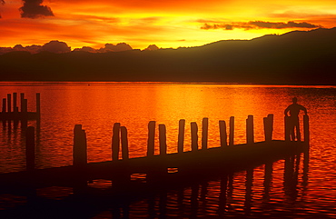 A man on a jetty overlooking Lake Windermere at sunset, Ambleside, Lake District, Cumbria, England, United Kingdom, Europe