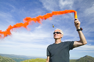 Member of the Langdale Ambleside mountain rescue team attracts a helicopter to an injured walker on Bow Fell in the Lake District, Cumbria, England, United Kingdom, Europe