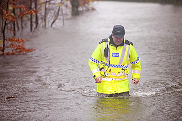 PC Paul Burke wading through floodwaters on Bog Lane near Ambleside, Cumbria, England, United Kingdom, Europe