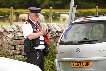 A parking attendant issues a ticket to a car parked on double yellow lines at Devils Bridge in Kirkby Lonsdale, Cumbria, England, United Kingdom, Europe