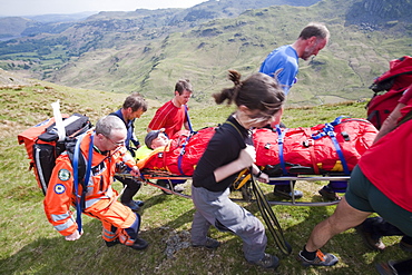 A man with a leg injury is stretchered towards an air ambulance by members of the Langdale Ambleside Mountain Rescue Team, above Grasmere, Lake District, Cumbria, England, United Kingdom, Europe