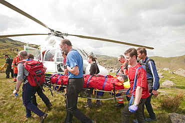 A man with a leg injury is stretchered towards an air ambulance helicopter by members of the Langdale Ambleside Mountain Rescue Team, above Grasmere, Lake District, Cumbria, England, United Kingdom, Europe