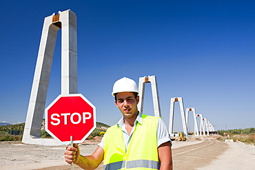 A workman stopping construction traffic where the railway crosses a road at a High Speed rail link being constructed between Antequera and Granada in Andalucia, Spain, Europe